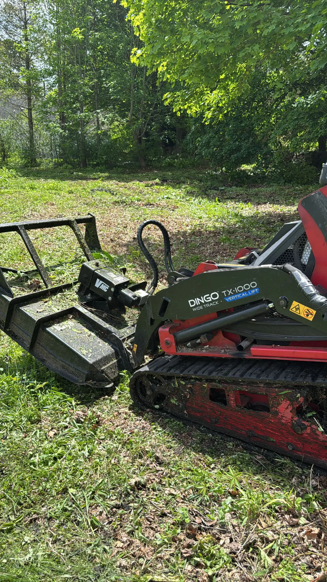 A mini skid steer with a brush-cutting attachment on a cleared lot
