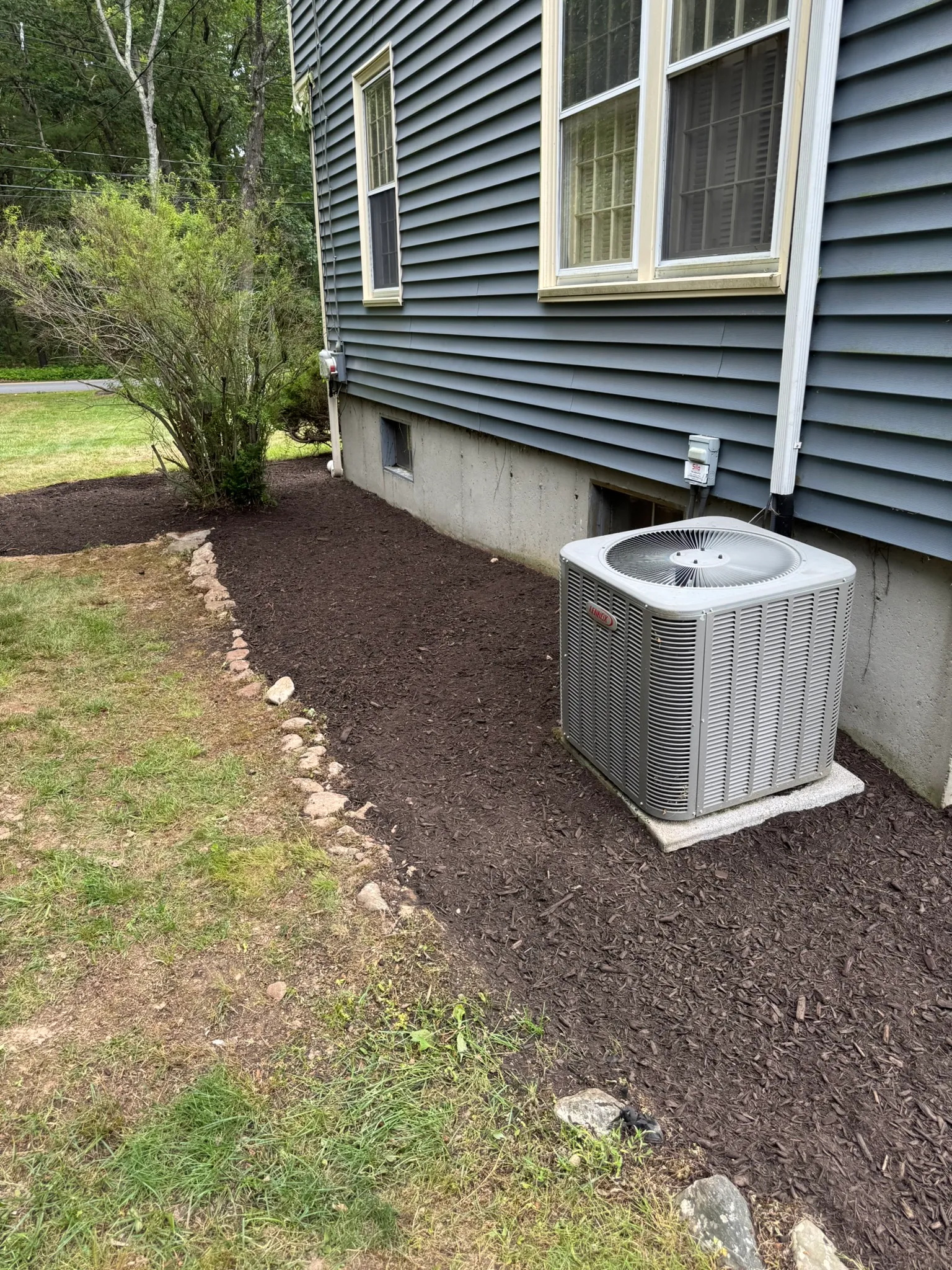 A mulched planting bed with stone edging running along a home foundation in Belmont, MA