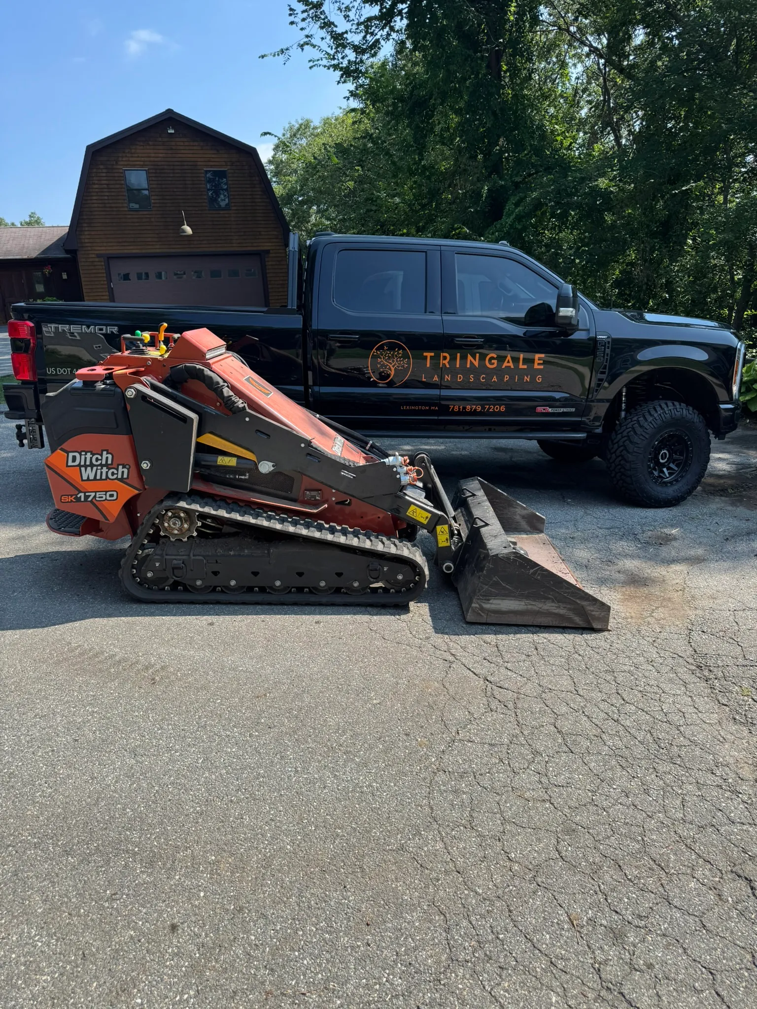 A Tringale Landscaping truck and mini skid steer staged on a driveway before a Concord, MA excavation job