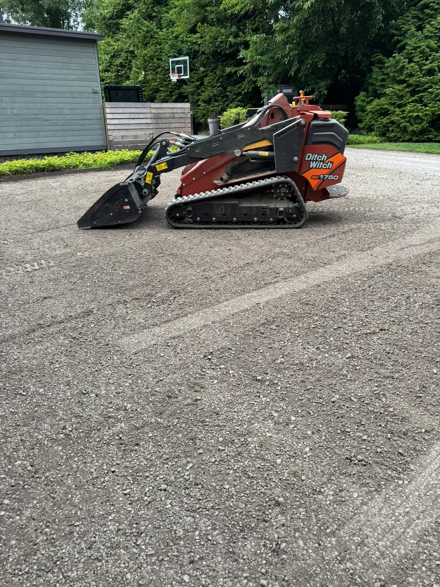 A compact mini skid steer working a narrow gravel driveway with tight access in Concord, MA