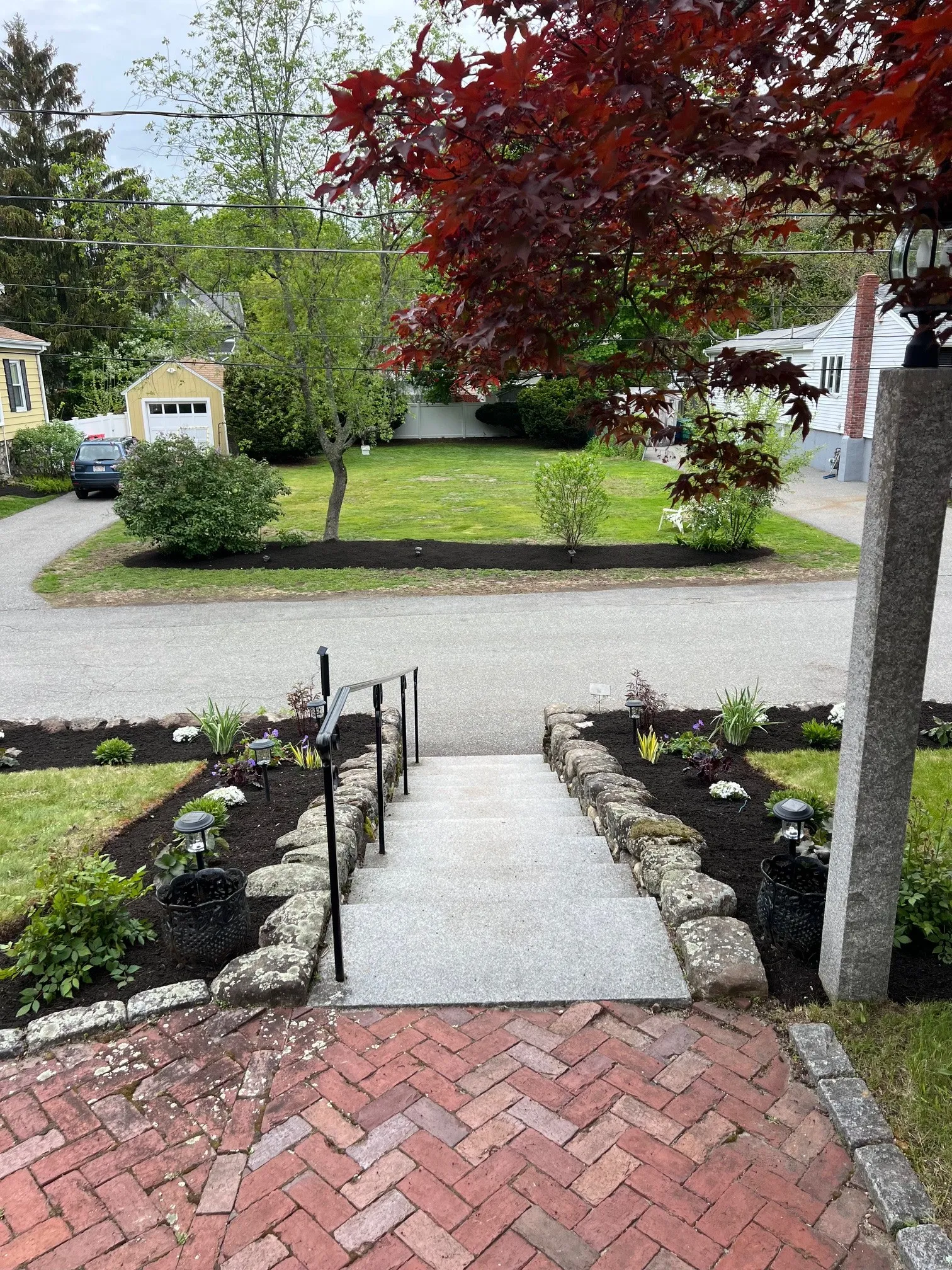 Granite front steps with fieldstone edging, a brick herringbone landing, and freshly mulched planting beds